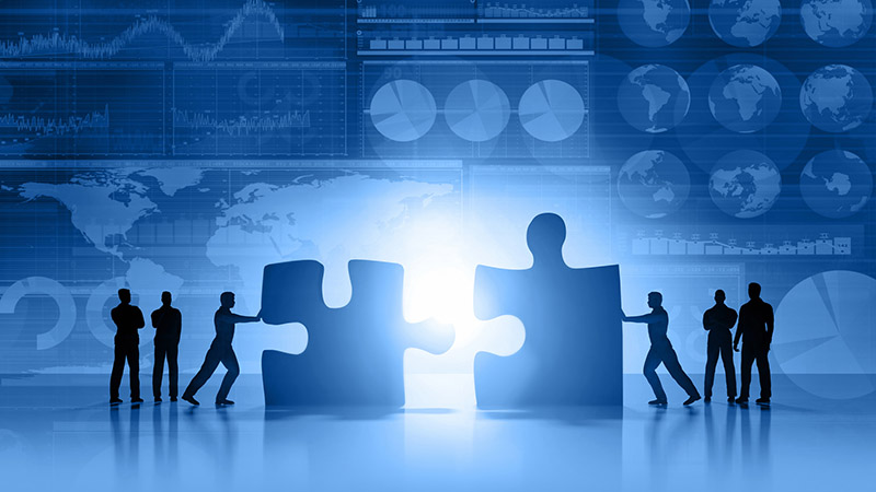 Silhouette of business people moving and joining pieces of jigsaw puzzle on a business and stock market blue background, with charts, diagrams, world maps and data arranged on grid and tables. World maps showing continents and countries with economy data and growth diagrams. Light glowing from the center. Copy space on bottom.